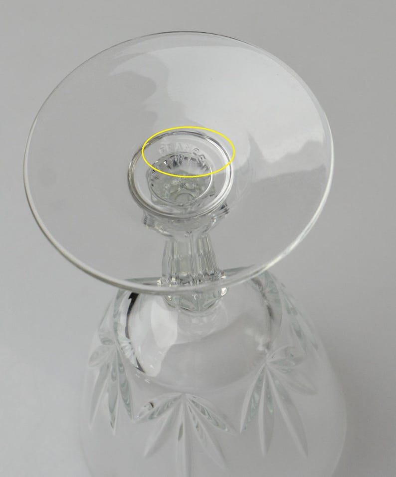 May include: Clear crystal wine glass with a round base and a detailed stem. The bowl of the glass features a starburst pattern. The base of the glass has the etched text "STAFFS".