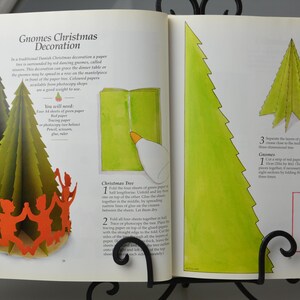 May include: A book with instructions on how to make a paper gnome Christmas decoration. The book shows a green paper gnome with a red hat and a green paper Christmas tree. The text on the page reads "Gnomes Christmas Decoration".