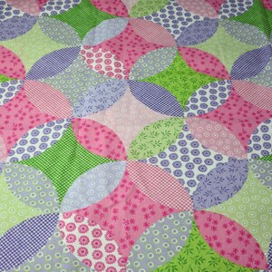 May include: A patchwork fabric with a repeating pattern of green, pink, and purple circles. The fabric has a variety of different patterns within the circles, including polka dots, floral designs, and gingham.