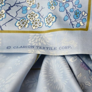 May include: A close-up of a blue fabric with a white floral pattern. The fabric has a gold border and the text "&copy; CLARION TEXTILE CORP." printed on it.