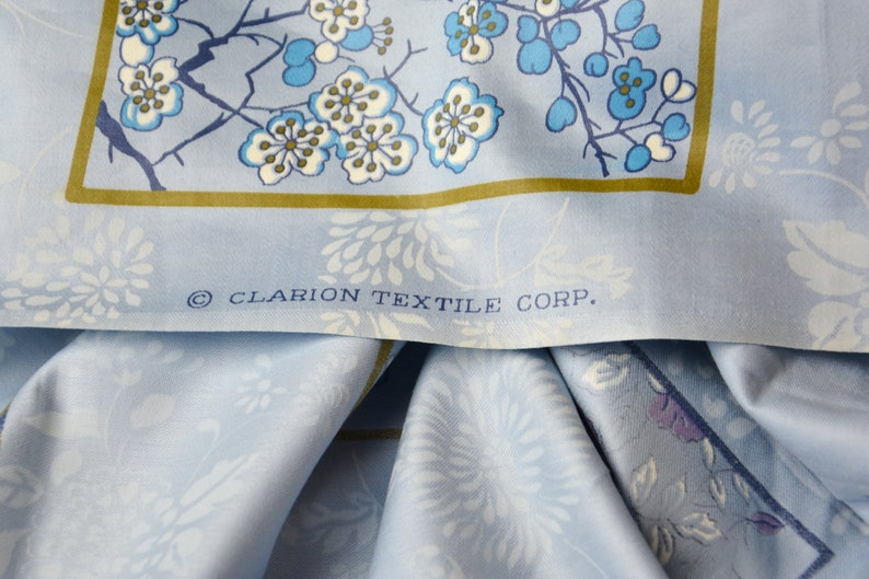 May include: A close-up of a blue fabric with a white floral pattern. The fabric has a gold border and the text "&copy; CLARION TEXTILE CORP." printed on it.