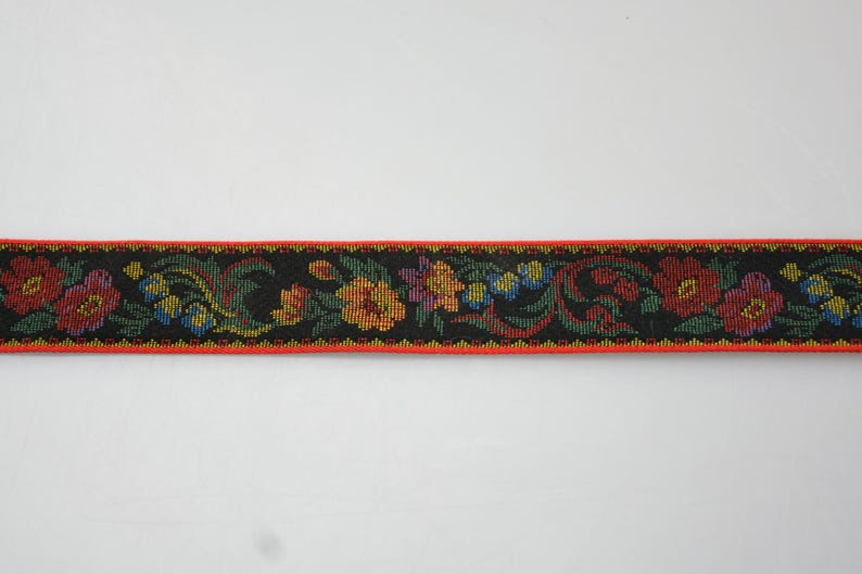 May include: Black ribbon trim with a floral pattern in red, orange, yellow, green, and blue. The trim has a red border.
