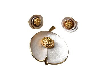 May include: A jewelry set consisting of a large brooch and two matching stud earrings. Each piece features a textured white, petal-like circular base with a raised, gold-toned, bumpy center that resembles a flower stamen or seed head.
