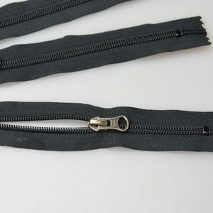 May include: Three black zipper closures with silver pull tabs. The zippers are laid out on a white surface.