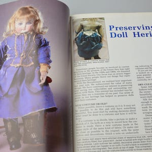 Pode incluir: Uma boneca de porcelana vintage com um vestido azul e dourado est&aacute; sentada em uma cadeira de madeira. A boneca tem um rosto delicado com olhos azuis pintados e bochechas coradas. A imagem &eacute; de um livro sobre a preserva&ccedil;&atilde;o do patrim&ocirc;nio das bonecas.
