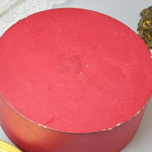 May include: A round, red cardboard box with a smooth, slightly worn surface. The box is empty and appears to be vintage.