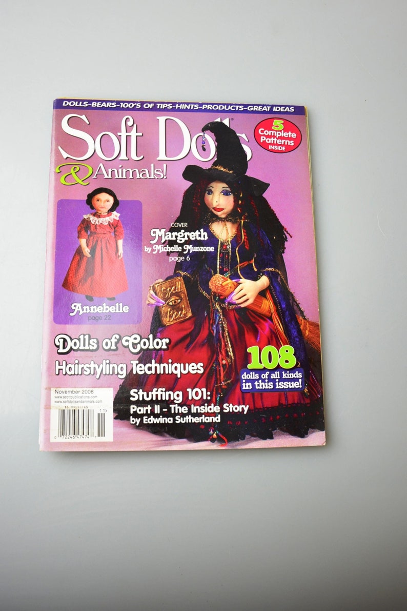 May include: Soft Dolls & Animals magazine cover featuring a witch doll with a purple and red dress, a black hat, and a book. The magazine cover also features a smaller doll with a red dress and a title that reads "Dolls of Color Hairstyling Techniques".