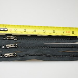 May include: Four black zipper closures with silver pulls, measured against a yellow tape measure. The tape measure reads 1 to 10 inches.