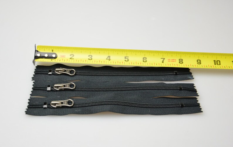 May include: Four black zipper closures with silver pulls, measured against a yellow tape measure. The tape measure reads 1 to 10 inches.