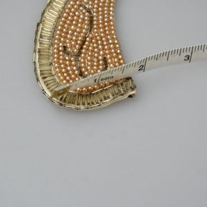May include: A gold-toned metal necklace with a design of small, light brown beads. The necklace is being measured with a tape measure, showing a length of 1 1/2 inches.