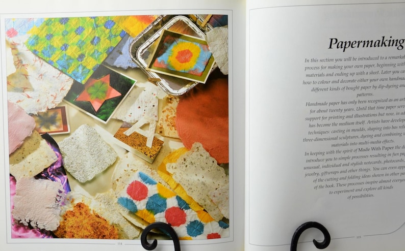 May include: A close-up of a book page with the title "Papermaking". The page features a colorful collage of handmade paper samples, including a star-shaped piece, a letter "A", and a tray of colorful paper. The text on the page describes the process of making handmade paper.