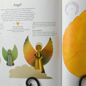 May include: A craft project for making a paper angel ornament. The instructions include using tracing paper, gift wrapping paper, scissors, and a felt tip pen. The finished angel is decorated with glitter, stars, or gold ribbon.