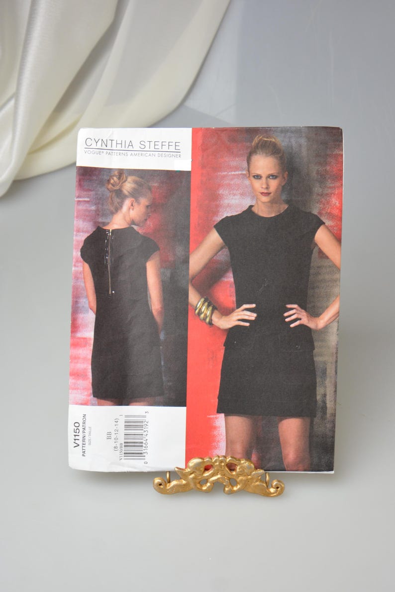 May include: A Cynthia Steffe Vogue Patterns American Designer dressmaking pattern. The pattern features a black dress with a zipper detail and a short skirt. The pattern number is V1150.