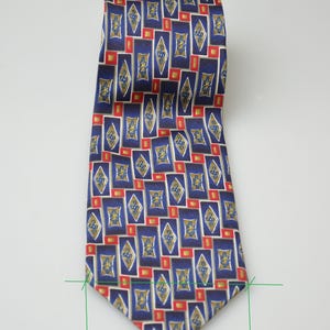 May include: A necktie featuring a repeating geometric pattern of blue rectangles and gold diamond shapes with small red squares. The tie has a width of 4 inches as indicated by the green measurement lines at the bottom of the fabric.