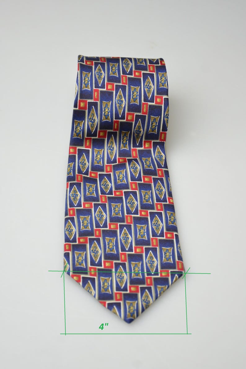 May include: A necktie featuring a repeating geometric pattern of blue rectangles and gold diamond shapes with small red squares. The tie has a width of 4 inches as indicated by the green measurement lines at the bottom of the fabric.