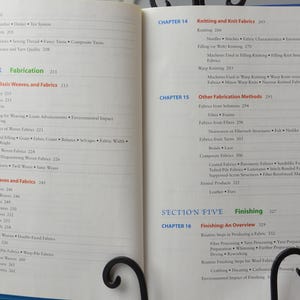 Puede incluir: Libro abierto con una cubierta azul y p&aacute;ginas blancas. El libro se titula "Fabricaci&oacute;n" y "Acabado". El libro est&aacute; abierto en dos p&aacute;ginas con texto sobre tejido, tejido de punto y otros m&eacute;todos de fabricaci&oacute;n de tejidos.