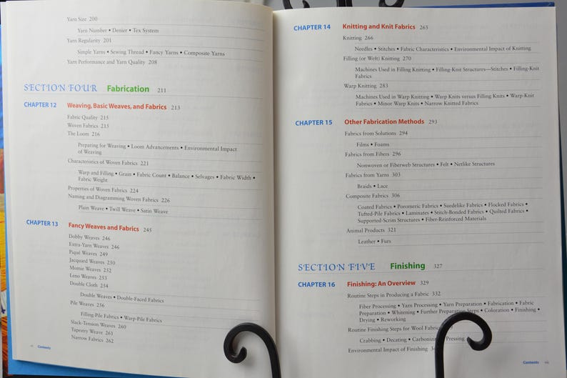 Puede incluir: Libro abierto con una cubierta azul y p&aacute;ginas blancas. El libro se titula "Fabricaci&oacute;n" y "Acabado". El libro est&aacute; abierto en dos p&aacute;ginas con texto sobre tejido, tejido de punto y otros m&eacute;todos de fabricaci&oacute;n de tejidos.