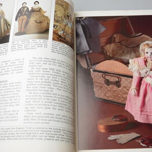 Pode incluir: Uma boneca vintage vestida com um vestido rosa com detalhes em renda branca e uma faixa branca. A boneca est&aacute; segurando uma pequena bolsa branca e est&aacute; de p&eacute; ao lado de um ba&uacute; de madeira com uma tampa de padr&atilde;o marrom e branco. A boneca est&aacute; usando sapatos brancos e uma faixa de cabe&ccedil;a branca.