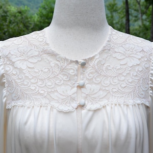 May include: Cream-colored nightgown with a delicate lace yoke and three small buttons. The long-sleeved gown is made of a smooth, silky fabric. The lace features a floral pattern.