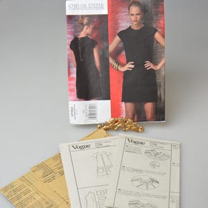 May include: A Cynthia Steffe Vogue sewing pattern, V1150, featuring a black dress design. The image includes pattern instructions and a gold-colored decorative element.