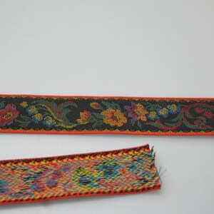 May include: Two pieces of red and black woven ribbon with floral patterns. The ribbon has a black background with red, yellow, green, and blue flowers.