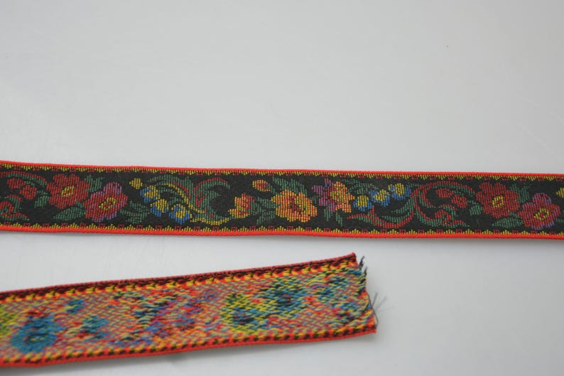May include: Two pieces of red and black woven ribbon with floral patterns. The ribbon has a black background with red, yellow, green, and blue flowers.