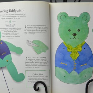 May include: Instructions for making a dancing teddy bear puppet. The instructions include a diagram of the teddy bear puppet and the steps to create it. The teddy bear is green and blue with a yellow bow tie.