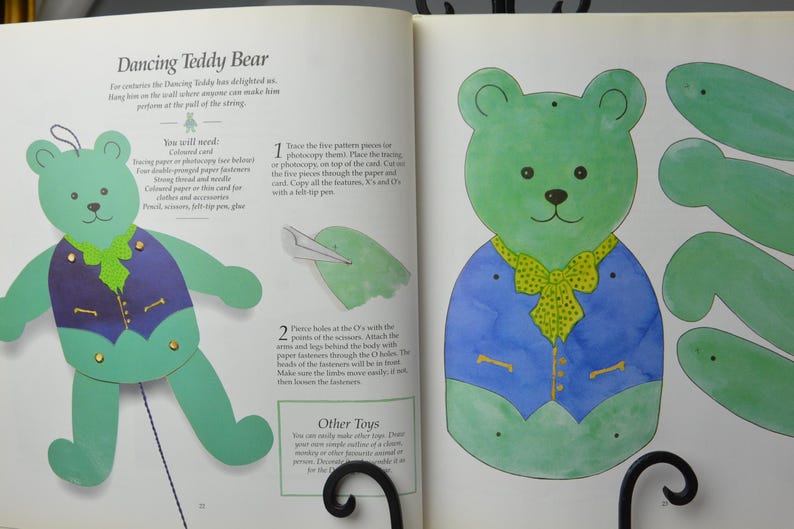 May include: Instructions for making a dancing teddy bear puppet. The instructions include a diagram of the teddy bear puppet and the steps to create it. The teddy bear is green and blue with a yellow bow tie.