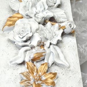 May include: White and gold floral wall decor with raised 3D flowers. The flowers are painted in a distressed white finish with gold accents.