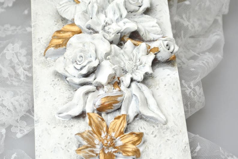 May include: White and gold floral wall decor with raised 3D flowers. The flowers are painted in a distressed white finish with gold accents.