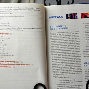 Puede incluir: Un libro abierto con fondo blanco y texto negro. El libro se titula "Textiles" y el texto trata sobre la filosof&iacute;a del libro, que es proporcionar a los estudiantes un conocimiento b&aacute;sico de los textiles para que comprendan c&oacute;mo se producen los textiles y c&oacute;mo se incorporan las caracter&iacute;sticas de rendimiento apropiadas en los materiales y productos. El libro tambi&eacute;n trata sobre la importancia de la comunicaci&oacute;n y la comprensi&oacute;n de los materiales textiles a lo largo de la cadena de suministro. Una comprensi&oacute;n s&oacute;lida de los componentes textiles, las hilazas, las telas y los acabados, y sus relaciones entre sus componentes, es necesaria para mejorar el rendimiento del producto en muchas carreras en las industrias textil, de la confecci&oacute;n y del hogar. El libro trata sobre las contribuciones de cada componente a un producto textil.