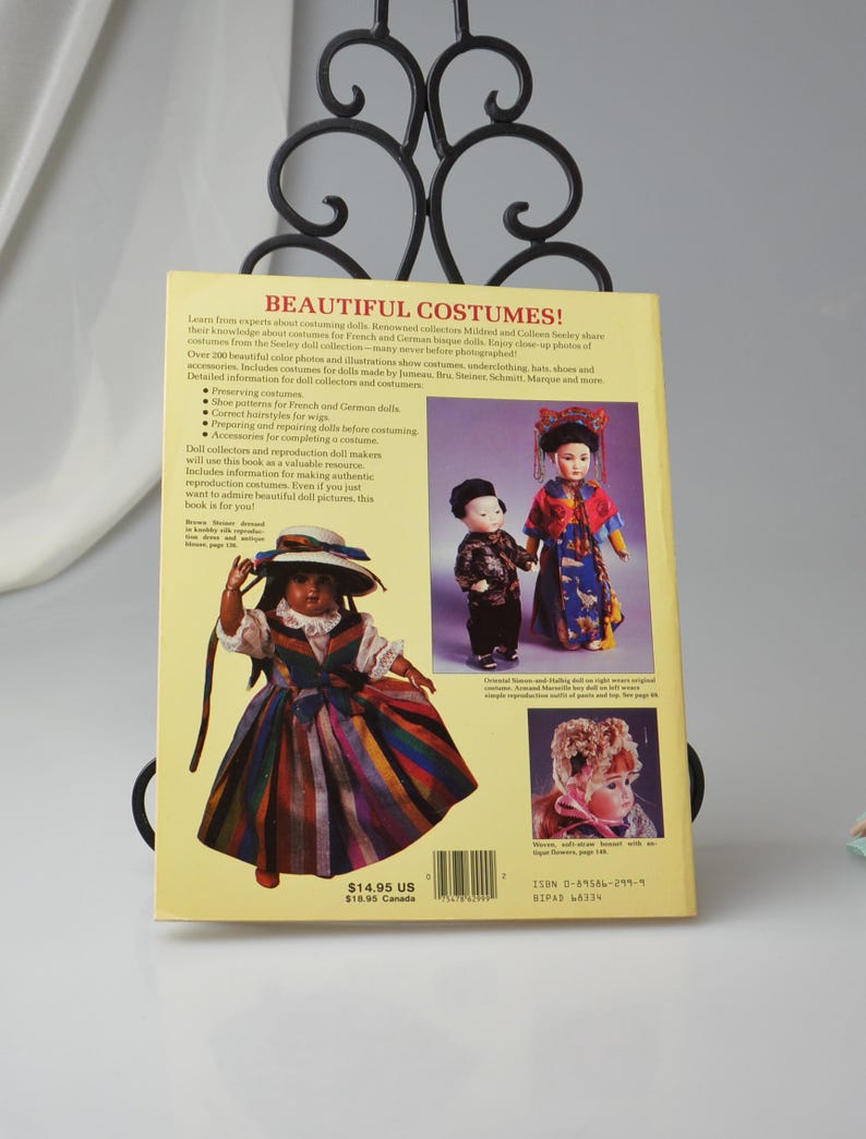 Pode incluir: Capa de um livro com o t&iacute;tulo "Beautiful Costumes!"  Aprenda com especialistas sobre o figurino de bonecas.  A capa apresenta uma boneca com um vestido listrado colorido e um chap&eacute;u.  O livro inclui mais de 200 fotos e ilustra&ccedil;&otilde;es coloridas de trajes, roupas &iacute;ntimas, chap&eacute;us, sapatos e acess&oacute;rios para bonecas feitas por Jumeau, Bru, Steiner, Schmitt, Marque e muito mais.  O livro custa $ 14,95 US.