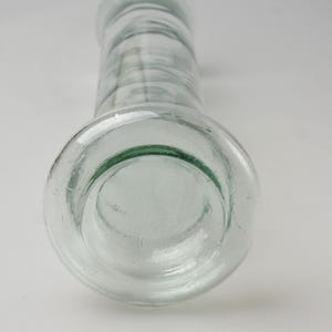 K&ouml;nnte beinhalten: Transparente Glasflasche mit breitem Boden und zylindrischem K&ouml;rper. Die Flasche hat einen abgerundeten Rand und eine leicht strukturierte Oberfl&auml;che. Das Glas ist transparent. Die Flasche wird wahrscheinlich zur Aufbewahrung von Fl&uuml;ssigkeiten verwendet.