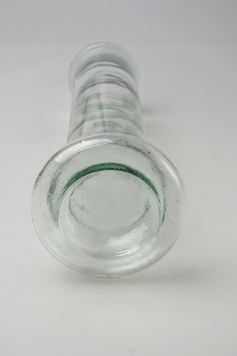 K&ouml;nnte beinhalten: Transparente Glasflasche mit breitem Boden und zylindrischem K&ouml;rper. Die Flasche hat einen abgerundeten Rand und eine leicht strukturierte Oberfl&auml;che. Das Glas ist transparent. Die Flasche wird wahrscheinlich zur Aufbewahrung von Fl&uuml;ssigkeiten verwendet.