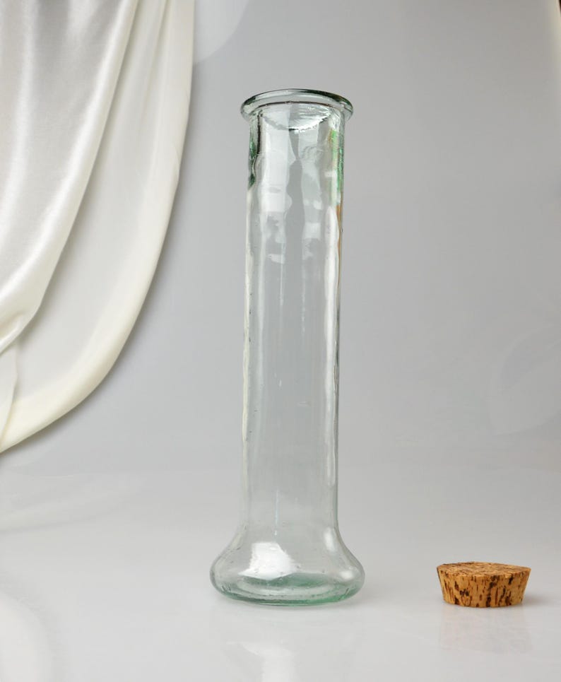 K&ouml;nnte beinhalten: Eine klare Glasvase mit ausgestelltem Boden und zylindrischem K&ouml;rper. Ein Korken liegt neben der Vase. Die Vase ist etwa 25 cm hoch.