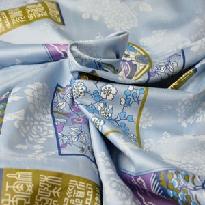 May include: Blue fabric with a repeating pattern of flowers, butterflies, and Chinese characters. The fabric is folded and draped, showing the pattern in detail.
