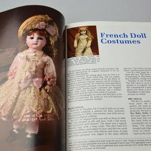 Pode incluir: Uma p&aacute;gina de livro vintage com uma foto de uma boneca de porcelana vestindo um vestido de renda branca e um chap&eacute;u de palha. O texto na p&aacute;gina diz "Trajes de Bonecas Francesas".