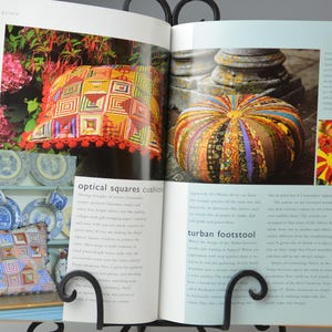 May include: An open book displaying images of a decorative pillow and a turban footstool. The pillow features a geometric design in red, orange, and yellow. The footstool is round with a striped pattern.