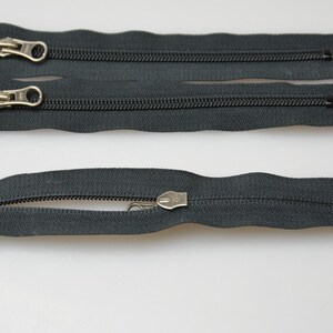May include: Three black zipper pulls with metal sliders. The zippers are separated and laid out on a white surface.