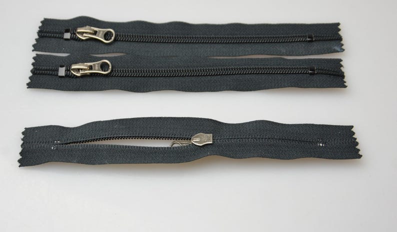 May include: Three black zipper pulls with metal sliders. The zippers are separated and laid out on a white surface.