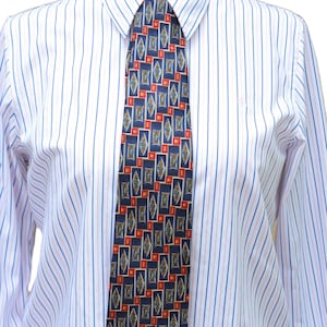 May include: A long-sleeved button-down shirt with vertical blue and pink stripes on a white background, worn with a necktie featuring a repeating pattern of dark blue rectangles, small red squares, and gold-toned diamond shapes.
