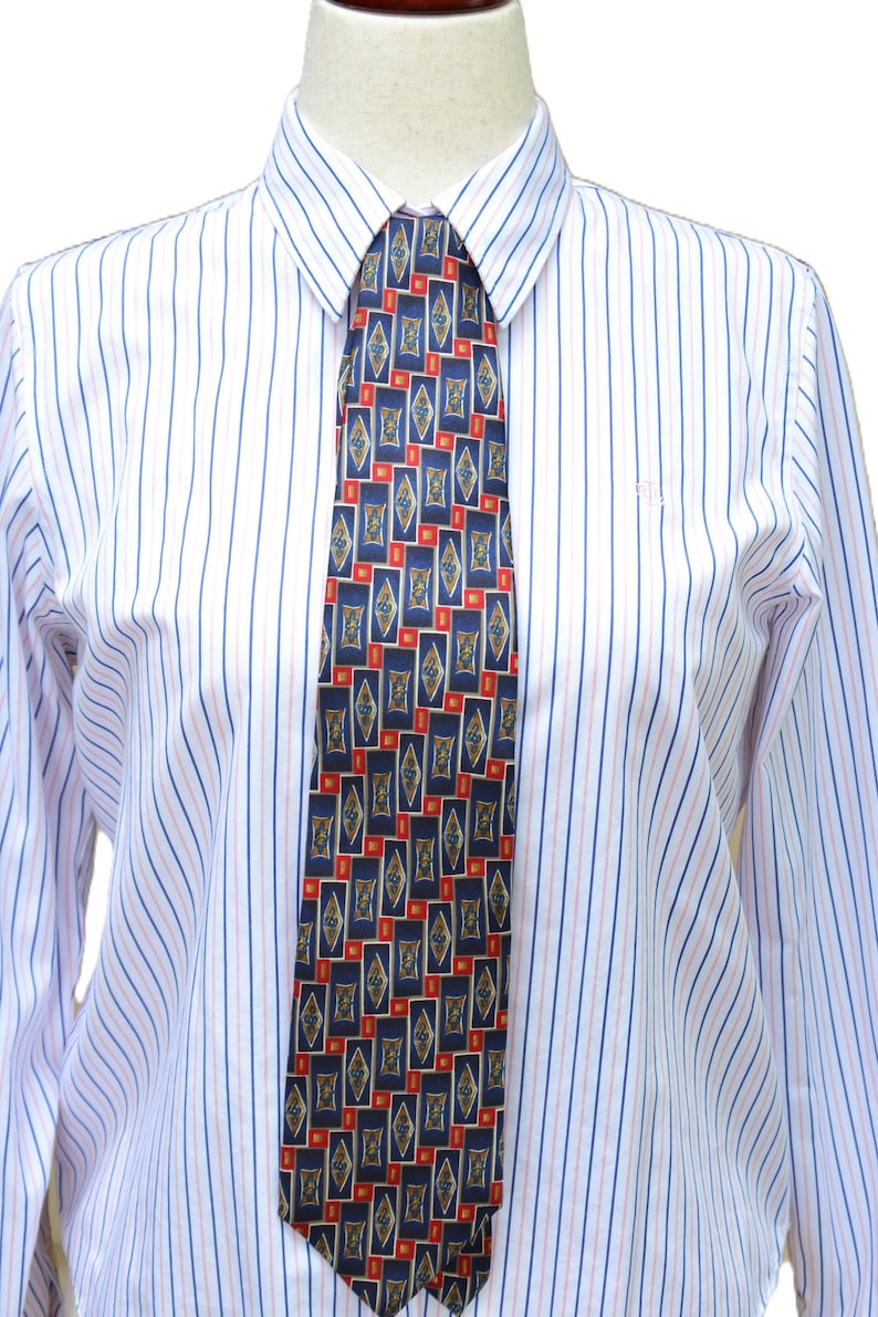 May include: A long-sleeved button-down shirt with vertical blue and pink stripes on a white background, worn with a necktie featuring a repeating pattern of dark blue rectangles, small red squares, and gold-toned diamond shapes.