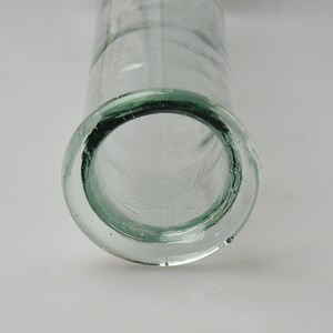 K&ouml;nnte beinhalten: Transparente Glasvase mit einer breiten, kreisf&ouml;rmigen &Ouml;ffnung und einem zylindrischen K&ouml;rper. Der Rand der Vase hat einen dezenten Gr&uuml;nton. Das Glas hat ein leicht strukturiertes Aussehen.