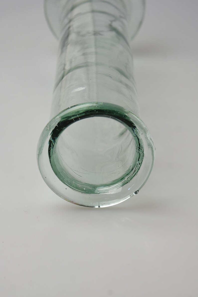 K&ouml;nnte beinhalten: Transparente Glasvase mit einer breiten, kreisf&ouml;rmigen &Ouml;ffnung und einem zylindrischen K&ouml;rper. Der Rand der Vase hat einen dezenten Gr&uuml;nton. Das Glas hat ein leicht strukturiertes Aussehen.