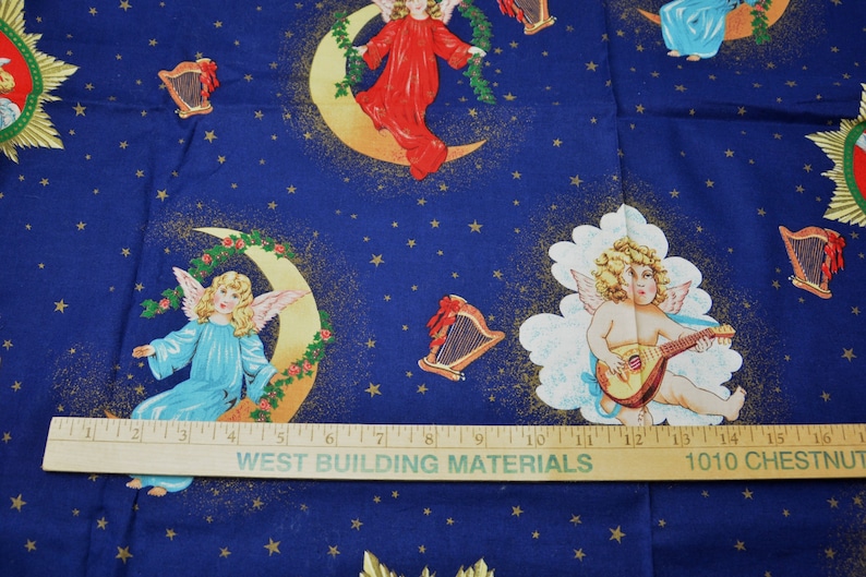 May include: Blue fabric with a celestial design featuring angels, moons, stars, and harps. Angels are depicted in various poses, some playing instruments, others seated on crescent moons. The fabric has a ruler with the text "WEST BUILDING MATERIALS" and "1010 CHESTNUT".