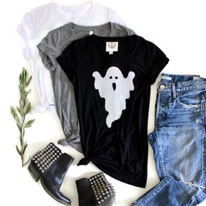 Op de afbeelding: Zwart T-shirt met een witte spookprint, blauwe jeans en zwarte enkellaarsjes met studs.
