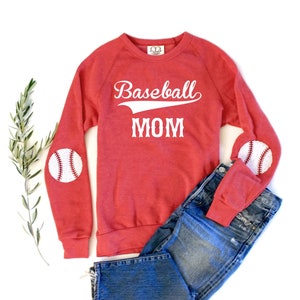 May include: Red sweatshirt with white text that says "Baseball Mom" and baseball patches on the elbows.