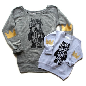 May include: Two gray sweatshirts with gold glitter crowns on the sleeves. The larger sweatshirt has a black silhouette of a monster with the text "I'll eat you up, I love you so" printed on it. The smaller sweatshirt has the same design but is a lighter gray.