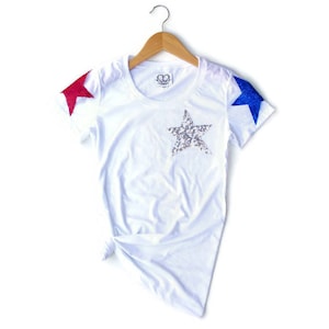 May include: White t-shirt with a silver sequined star on the front and red and blue stars on the sleeves.