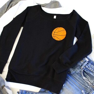 May include: Black sweatshirt with a large orange basketball graphic on the front. The sweatshirt has long sleeves and a relaxed fit.